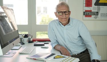 Designer ved skrivebord med materiale om piktogrammer og sikkerhedsskiltning.